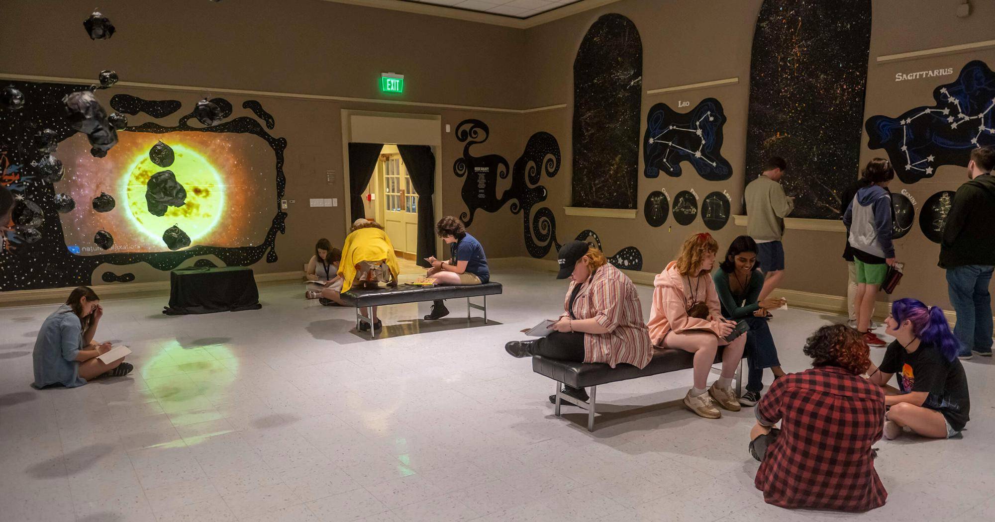 Image depicts students sitting in gallery painted to look like stars in space.