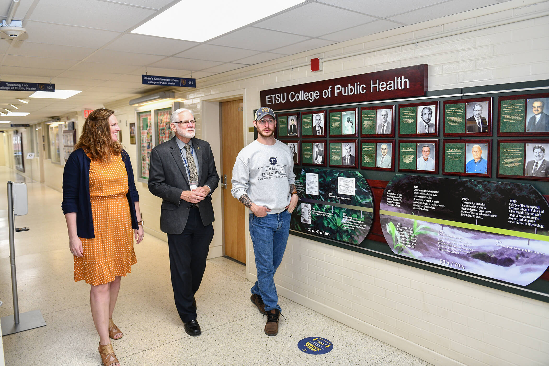 Dean Wycoff and two public health students, male and female, walk the hallway in Lamb Hall.
