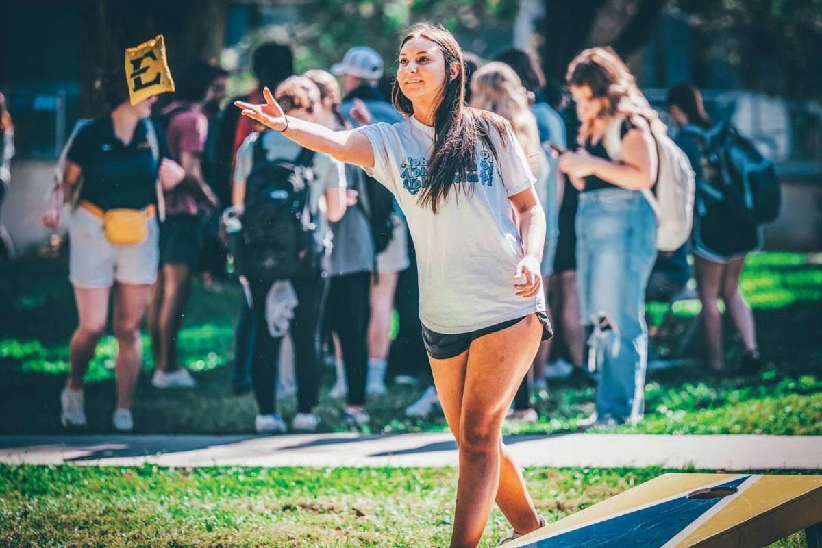 A photo of a student tossing a bean bag while playing cornhole.