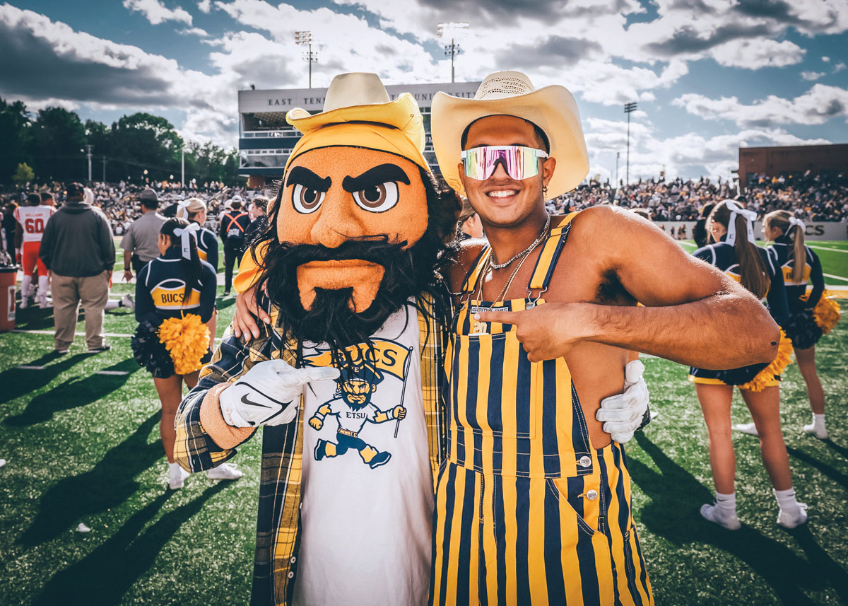 Bucky poses with an ETSU fan wearing blue and gold overalls at the football game.
