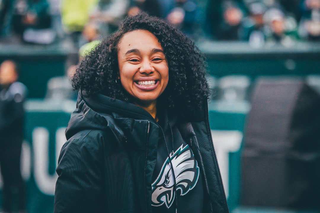 ETSU Alumna Autumn Lockwood smiling on the sideline of Philadelphia Eagles wearing a team hoodie and jacket.