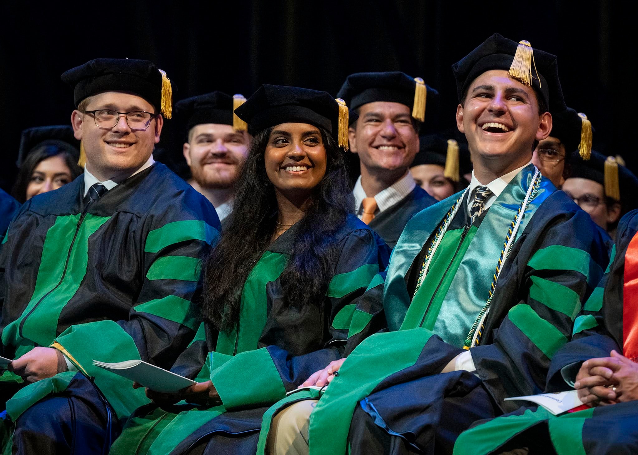 Graduating medical students smiling and laughing at the speaker on graduation day.