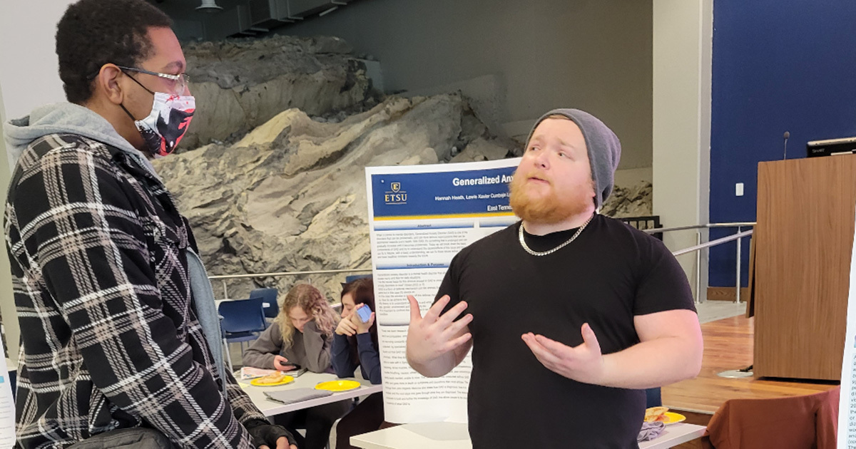 A man talks to another person at a table event in the DP Culp Student Cave.