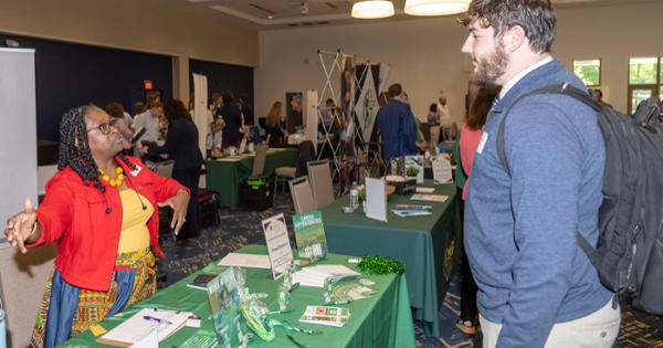 Female professional speaking to male student at event.