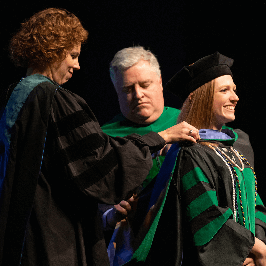 Two faculty members hooding the student on the stage.