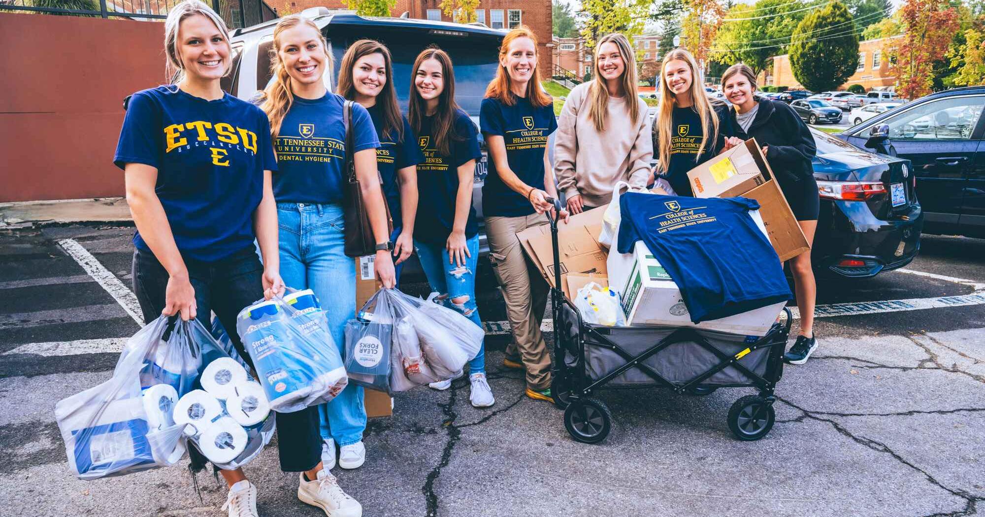 Students pose for a photo with supplies while unloading them outside of Lamb Hall.