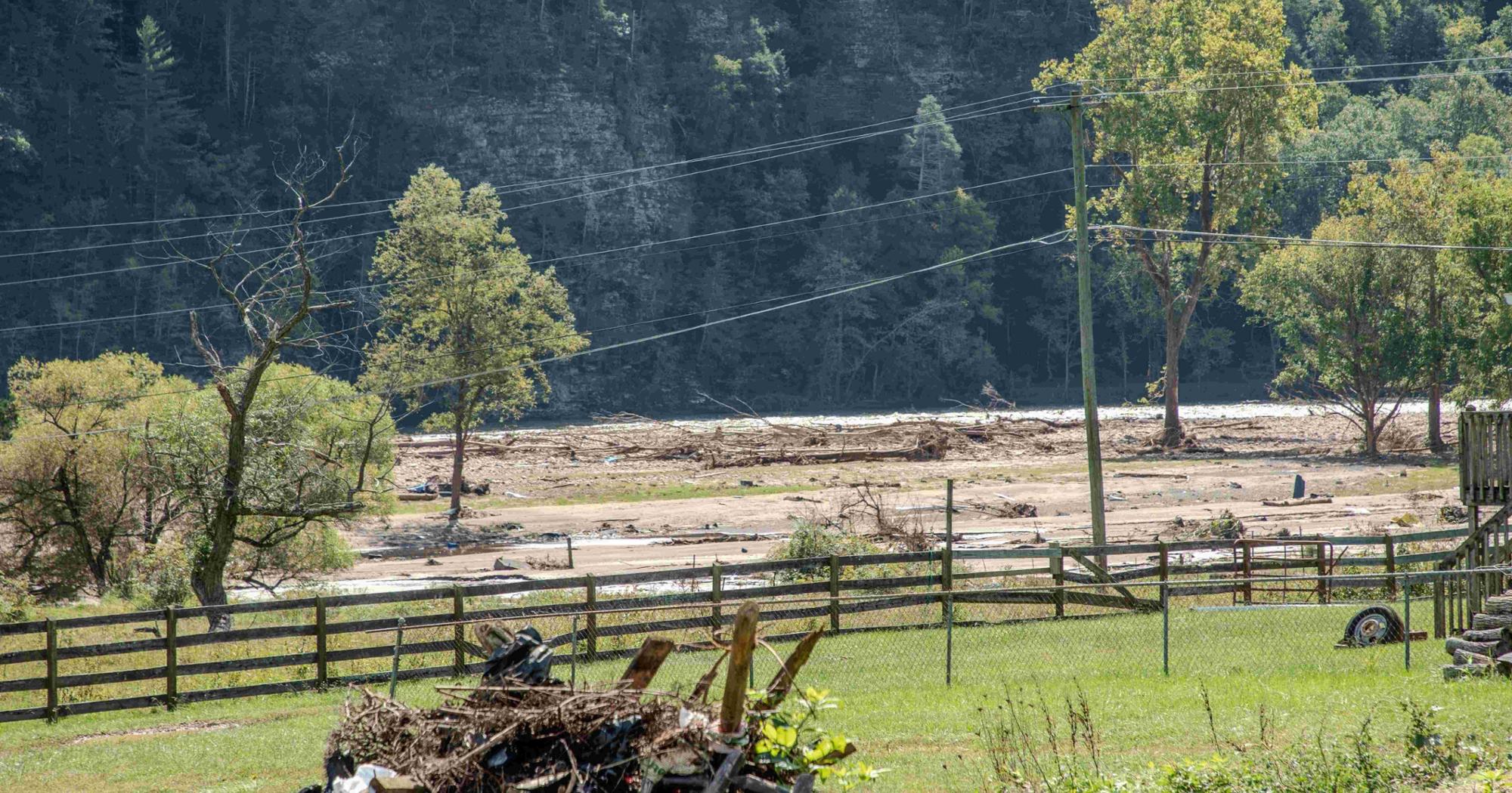 A photograph of a murky river with flood debris visible in the foreground.