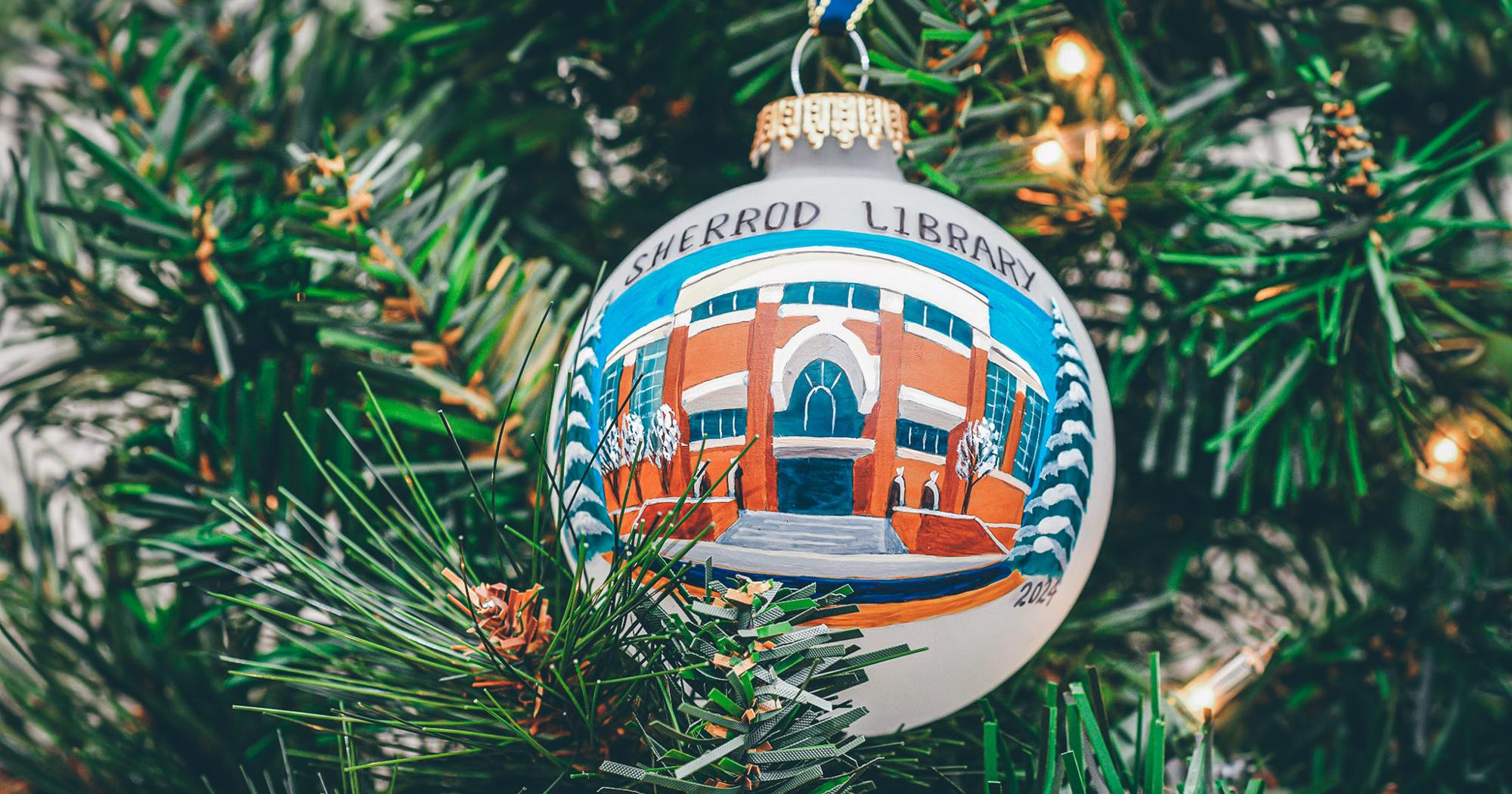 A glass, hand-painted ornament featuring the Charles C. Sherrod Library hanging on a Christmas Tree.