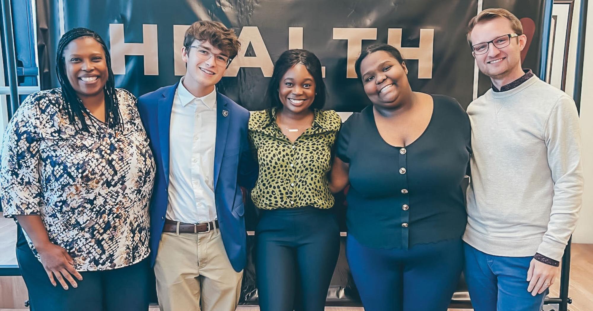 Group photo of students and faculty in front of a “HEALTH” banner.