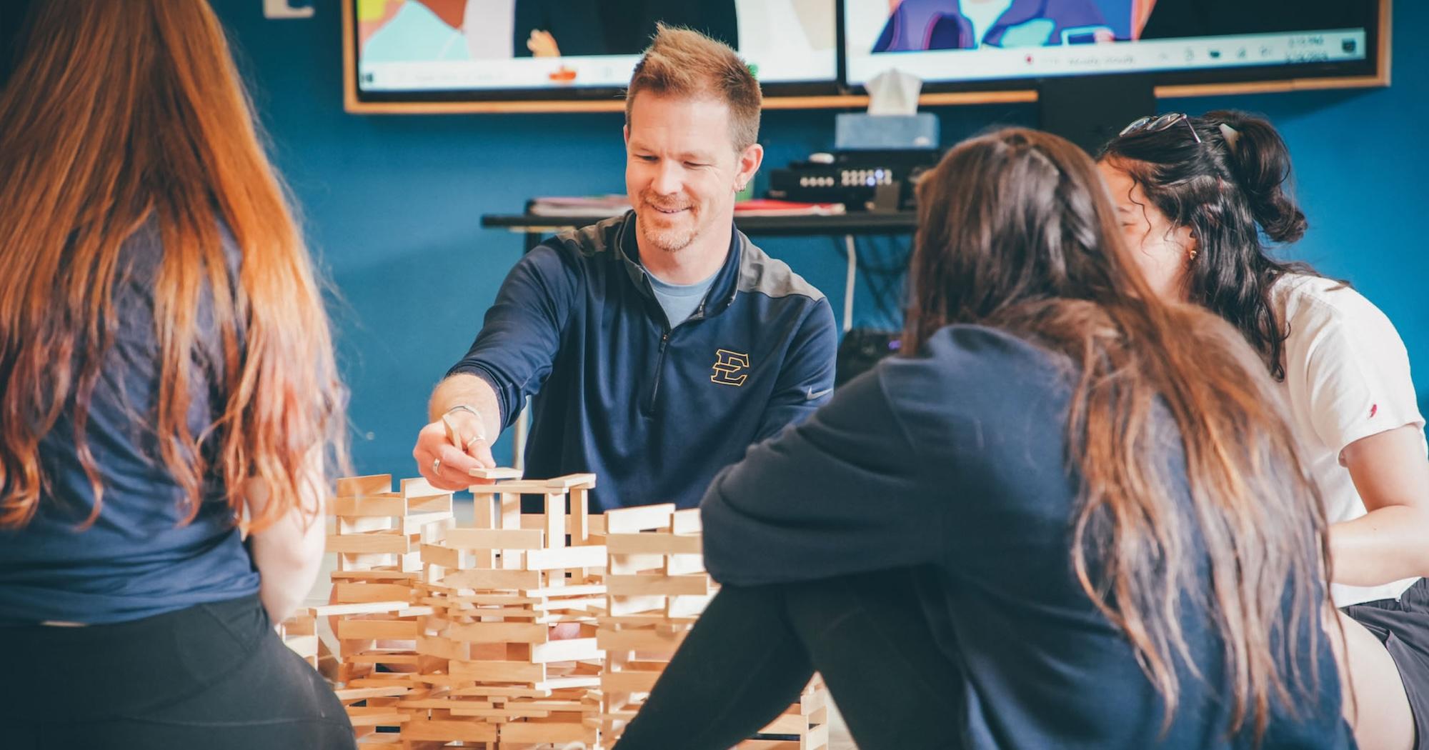 Person in ETSU jacket builds a wooden model with their hands.