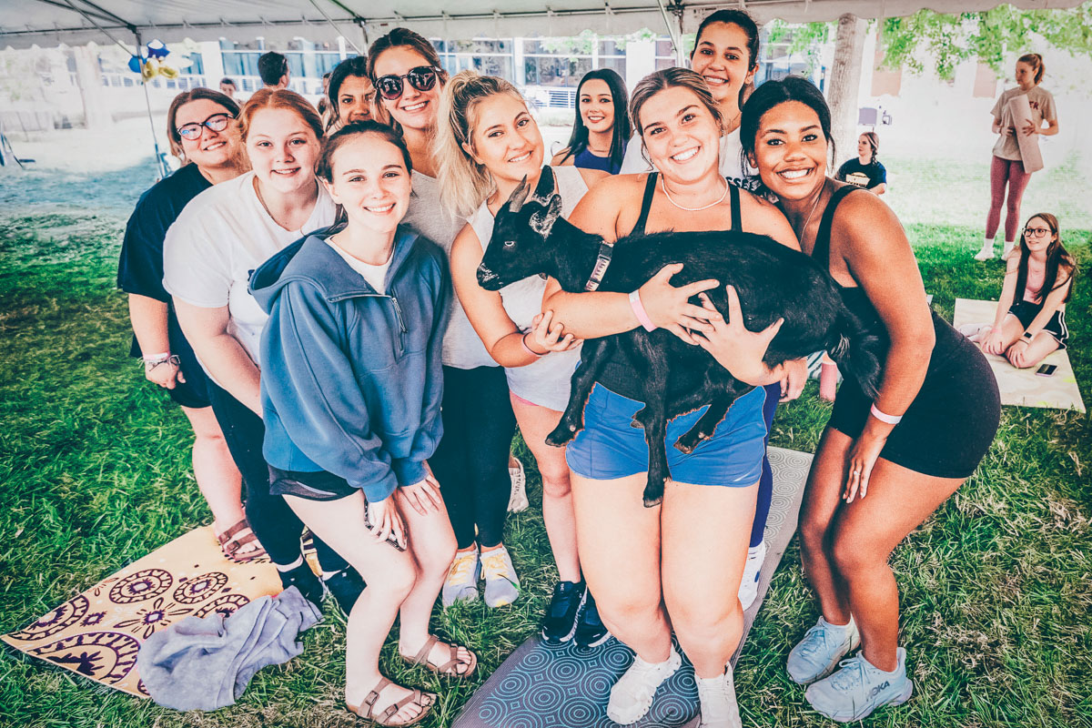 A photo of a group of students, and the student in the front is holding a goat.