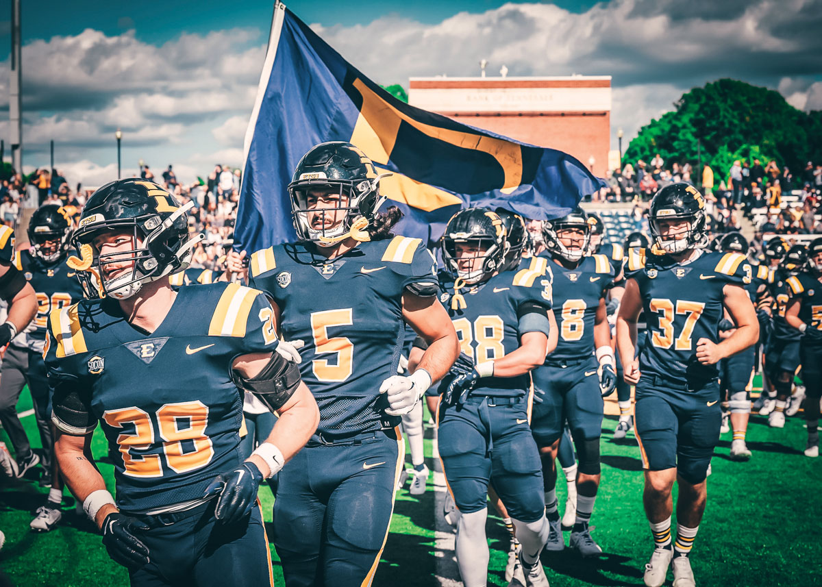 Football players run onto the field with the E flag.