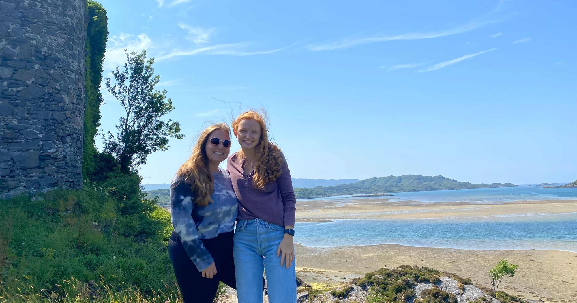 Two study abroad students by the coast and an old wall in England on a sunny day
