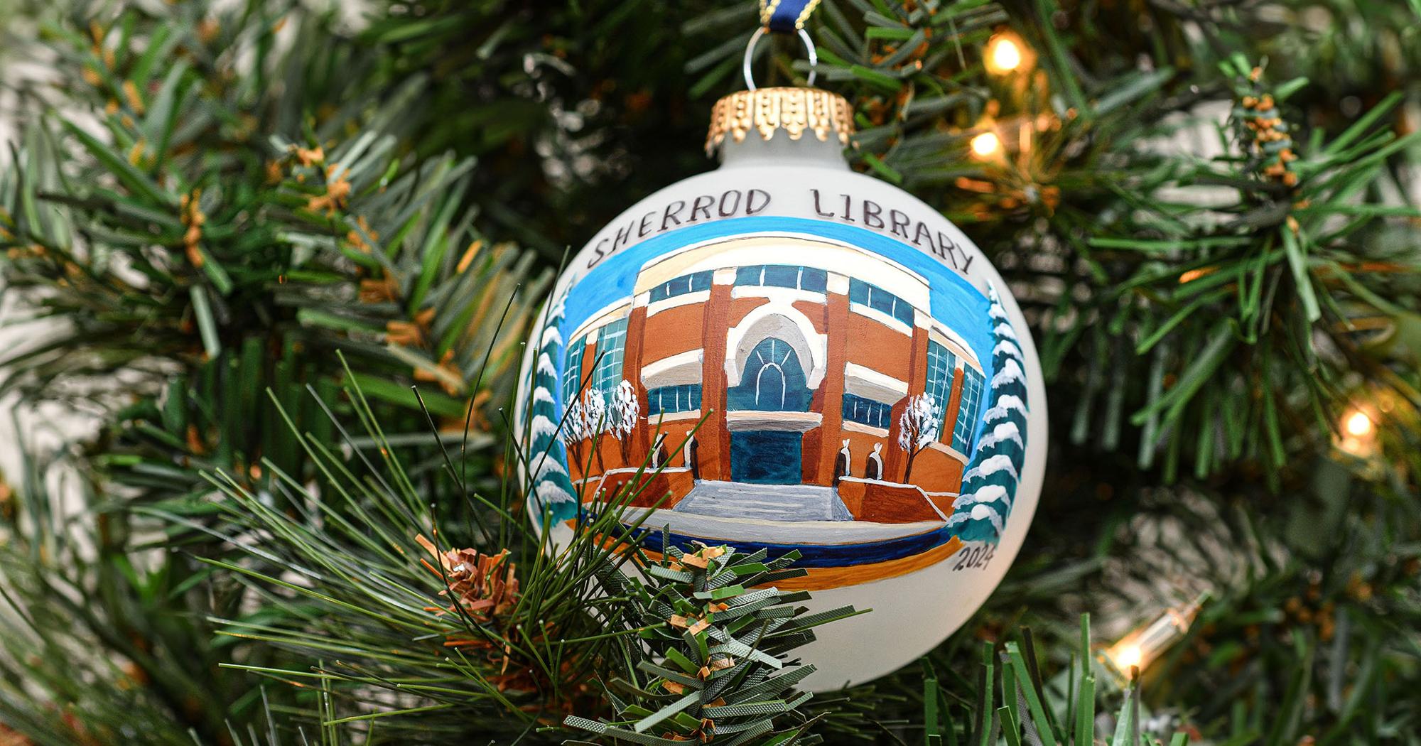 2024 ETSU Christmas Ornament, featuring a handpainted drawing of the Sherrod Library, hanging on a christmas tree branch.