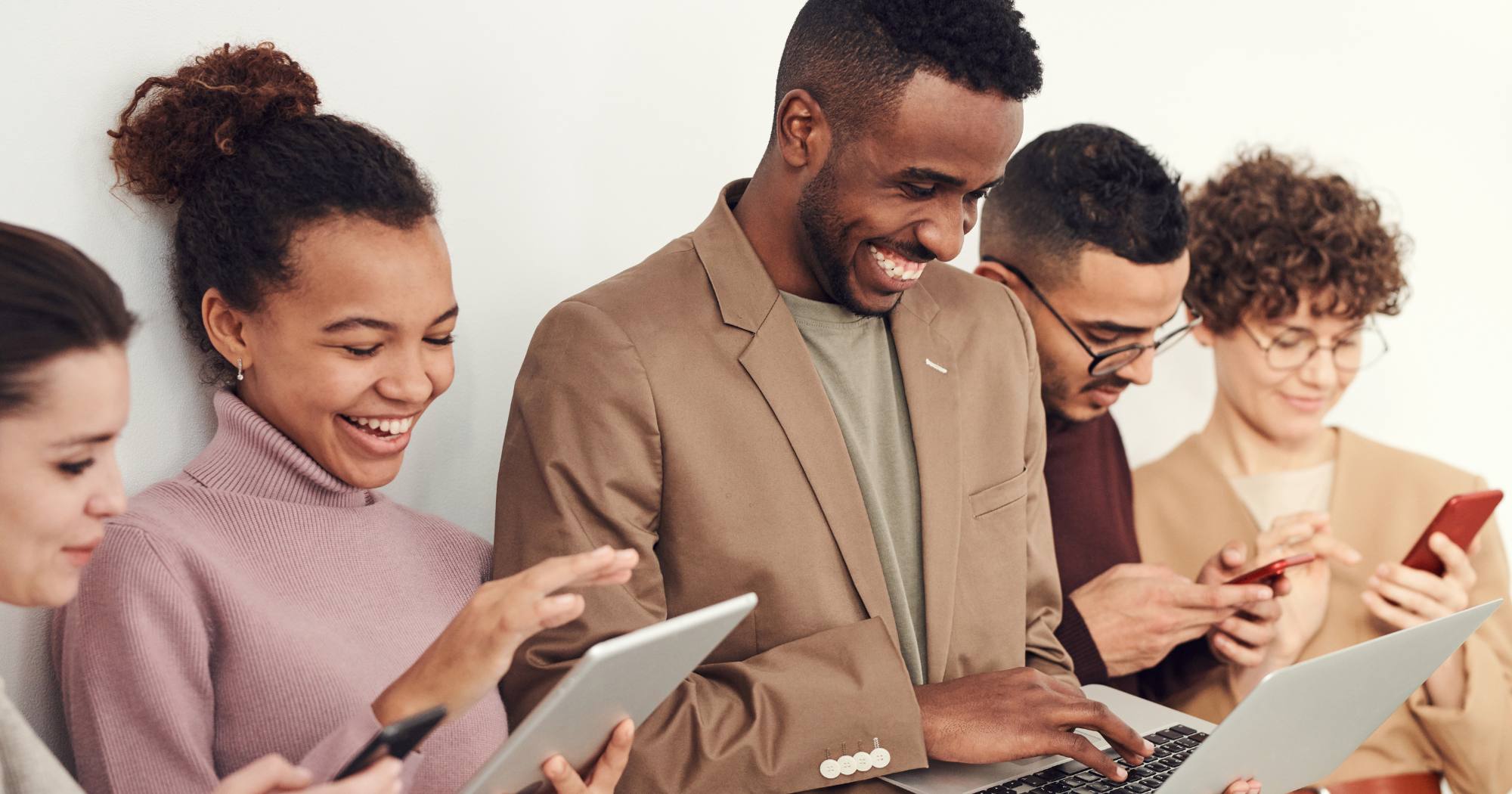 A group of people are holding electronic devices. They are looking at each other's screens and smiling.